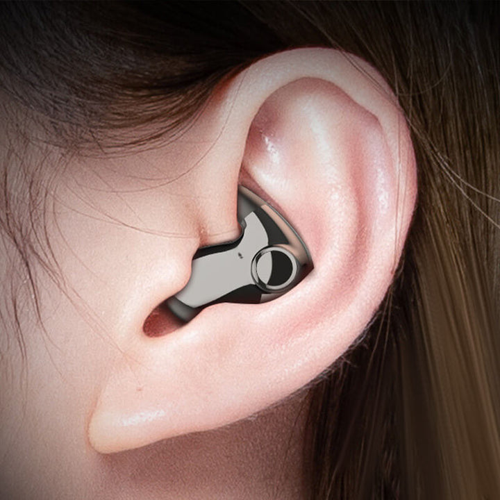 Nærbillede af en mørk metalgrå øretelefon, der sidder diskret i en kvindes øre 1