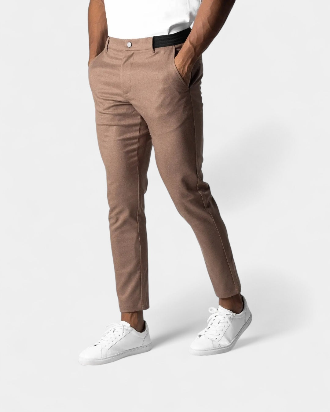 Model i brune smalle bukser med sort elastisk linning, hænder i lommerne og hvide sneakers 5