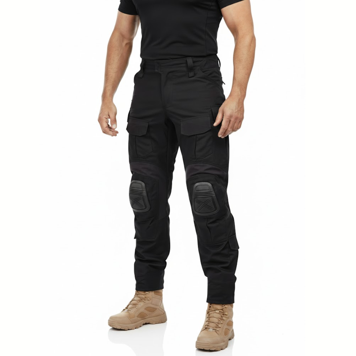 Mand i sort T-shirt og beige støvler viser de sorte cargobukser forfra, med lårlommer og knæbeskyttere. 2