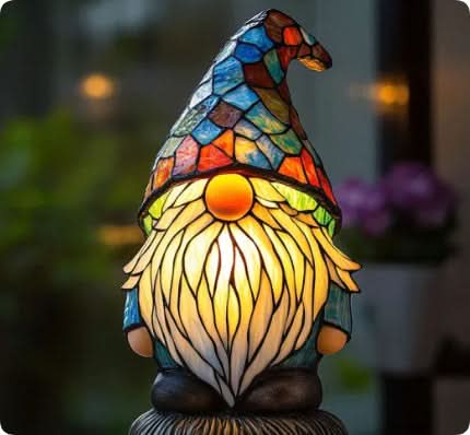 Lampe formet som en nisse med mosaikhue, hvidt skæg og orange næse, tændt mod sløret baggrund. 13