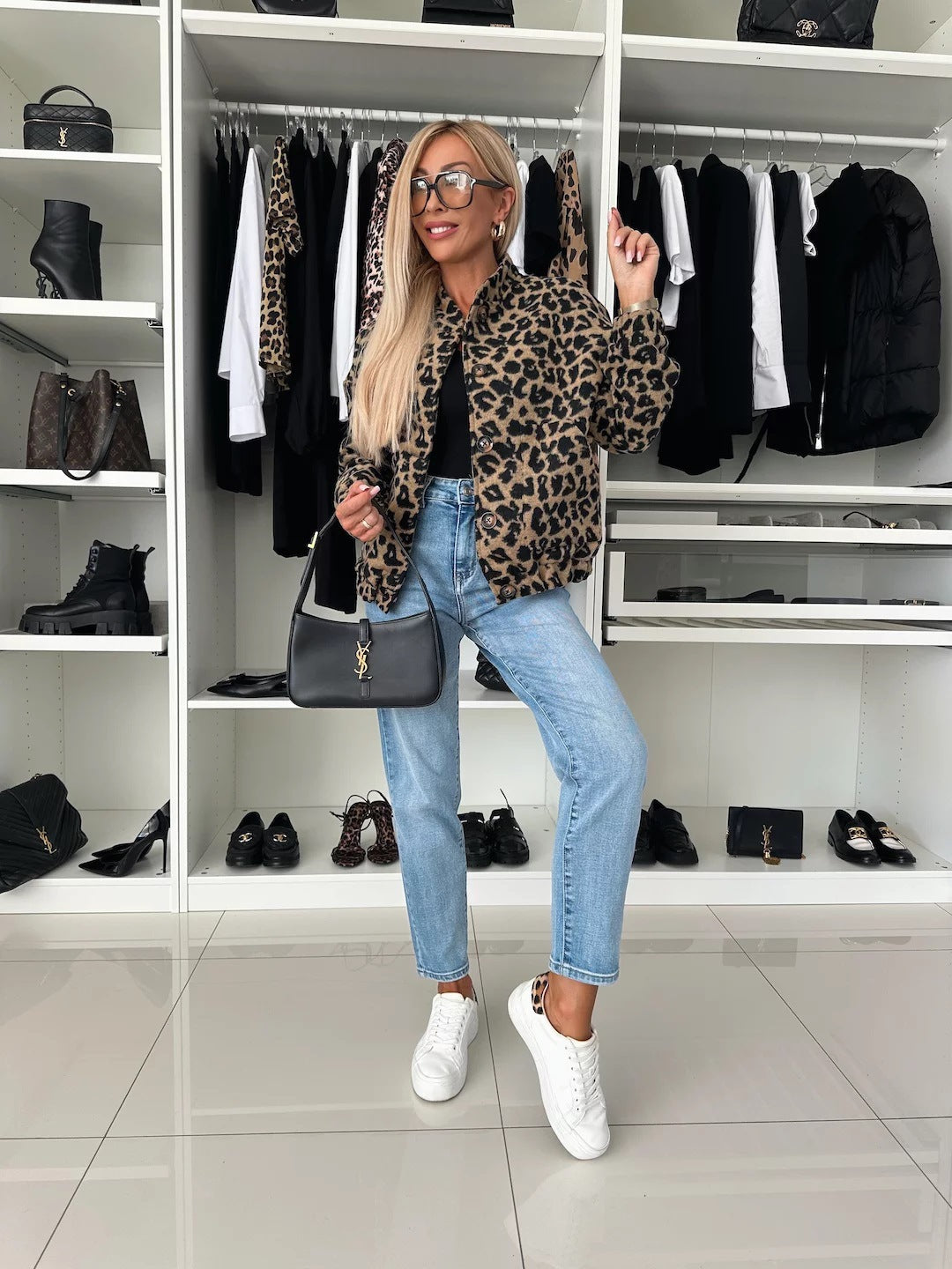 Helfigur af model i leopardbomberjakken med jeans, hvide sneakers og sort skuldertaske foran en åben garderobe med tøj og sko. 5