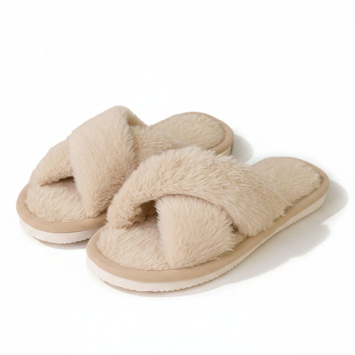 Par beige plysede hjemmesko med krydsede remme, vist fra siden på hvid baggrund med lys sål. 1