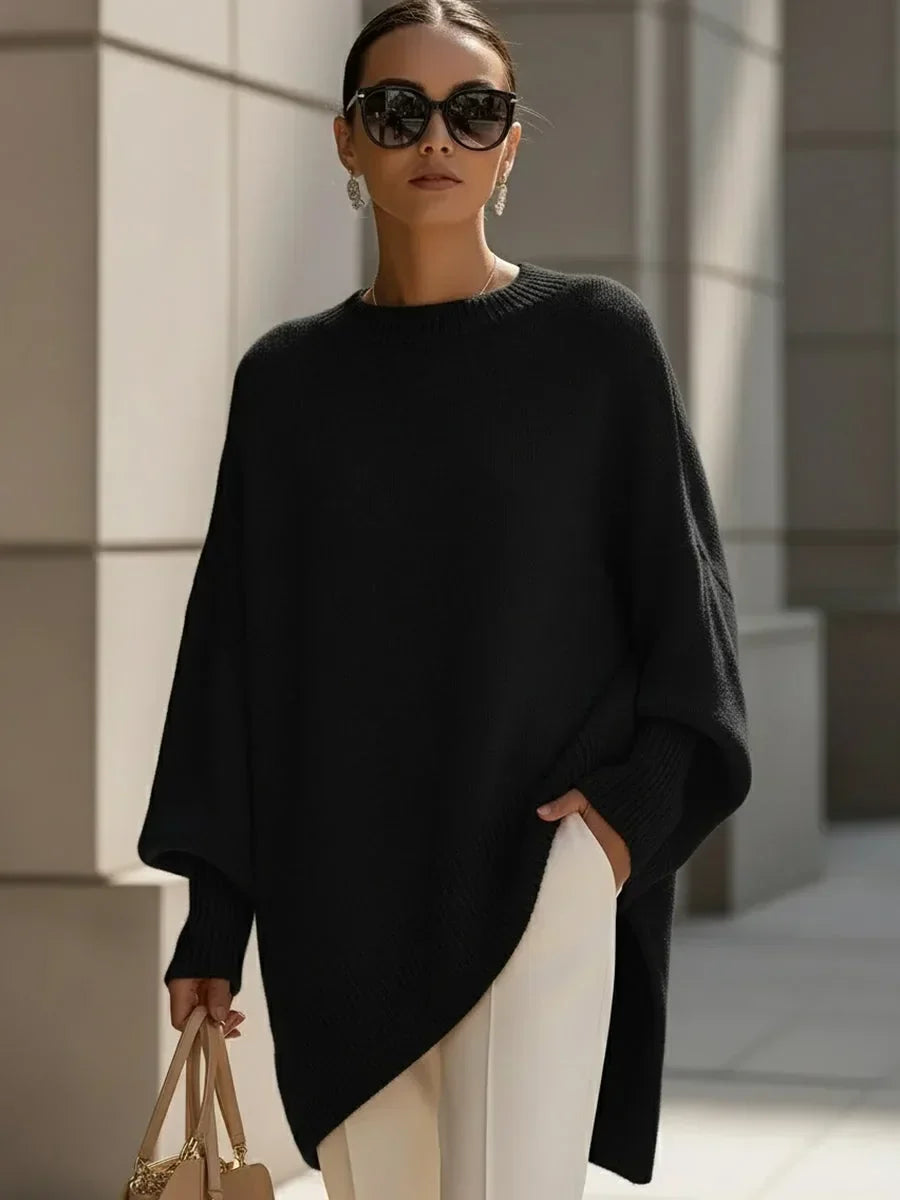 Model i sort oversize strikbluse med asymmetrisk kant, hvide bukser, solbriller og taske i hånden. 6