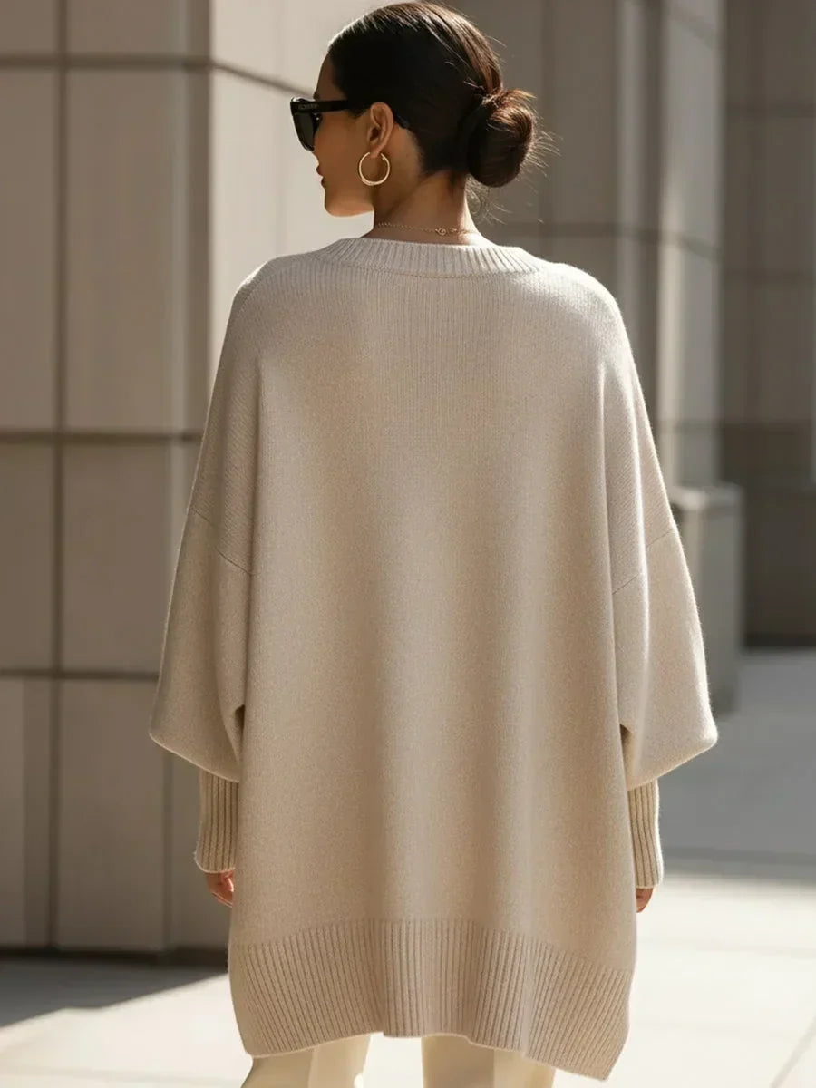 Model set bagfra i beige oversize strikbluse med ribkant forneden, hår i knold og solbriller. 4