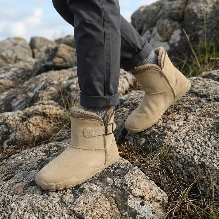 Beige støvler båret af person med mørke bukser og uldsokker på klipper udendørs 2