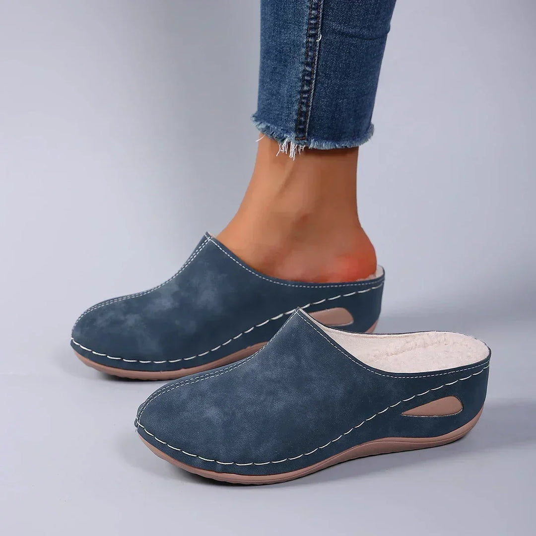 Blå tøfler båret med jeans, set fra siden, så den hvide fleecefor ved åbningen kan ses. 4