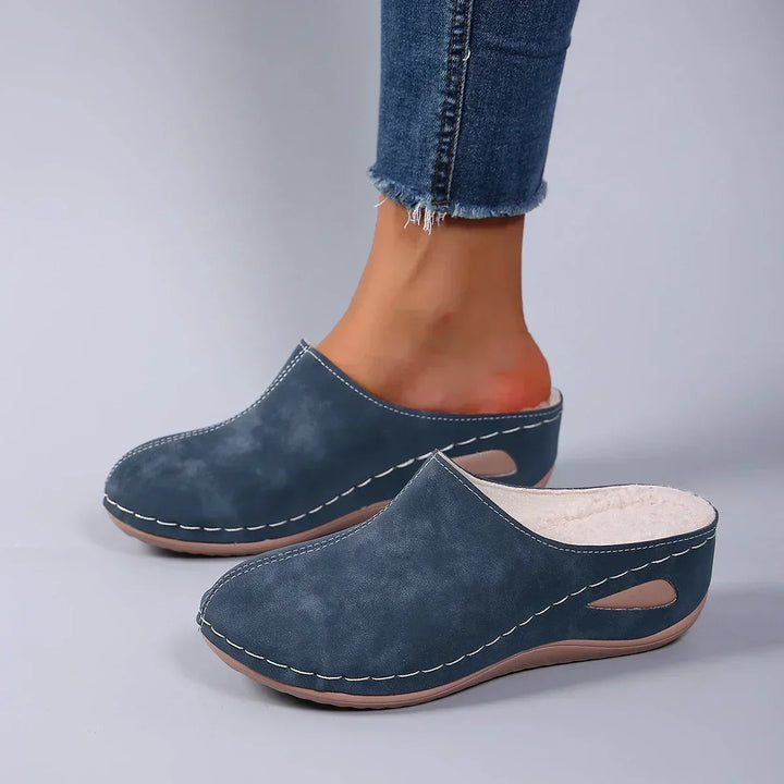 Blå tøfler båret med jeans, set fra siden, så den hvide fleecefor ved åbningen kan ses. 4