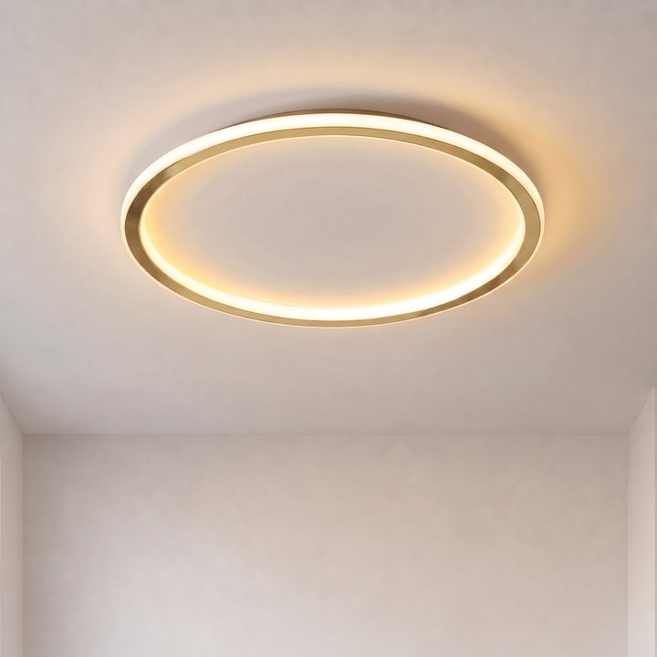 Tændt rund loftlampe med guldfarvet ring og varmt lys på hvidt loft, set nedefra 1