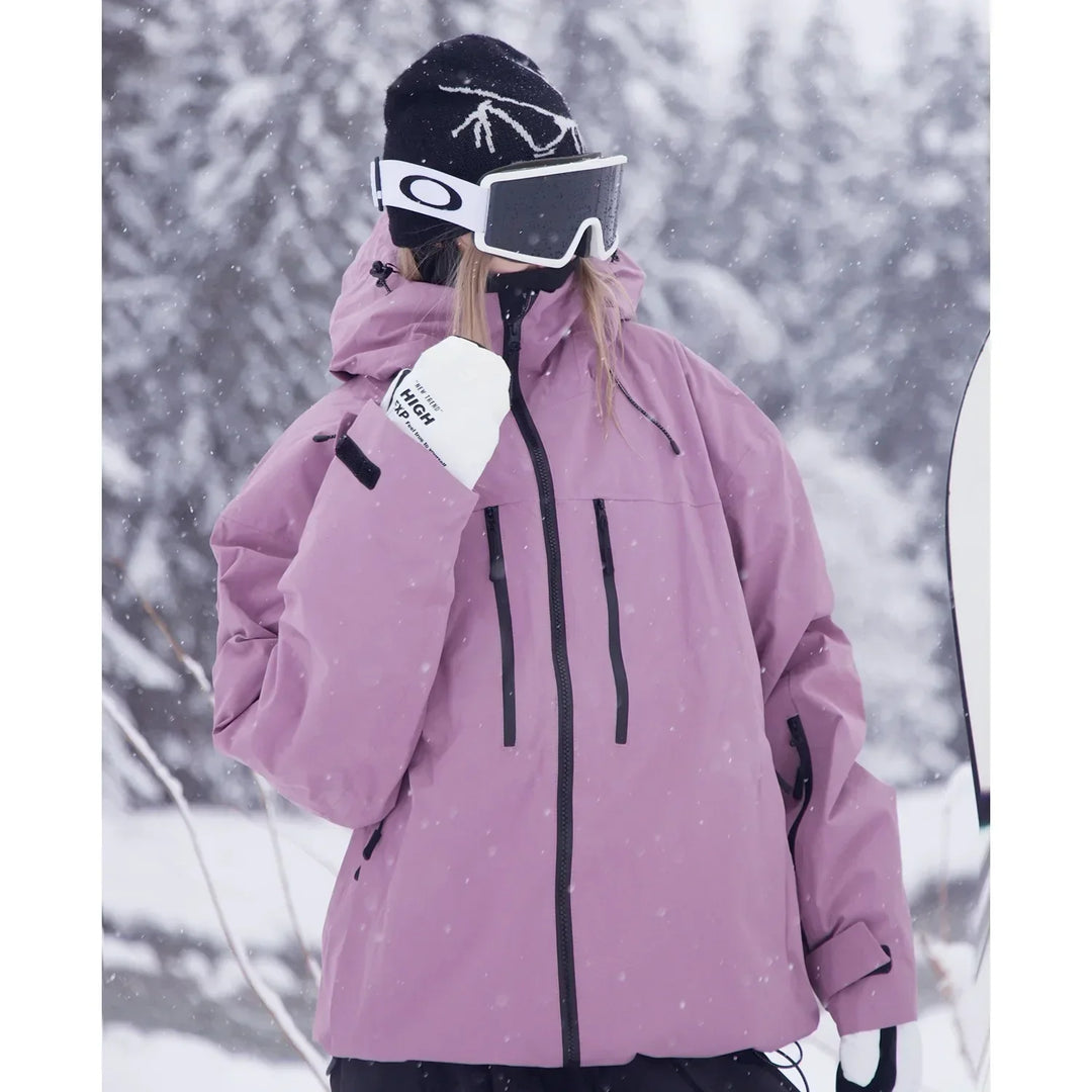 Tæt udsnit af model i lyslilla jakke med hætte, skibriller og hvide handsker, der løfter den ene hånd mod ansigtet i snevejr. 4
