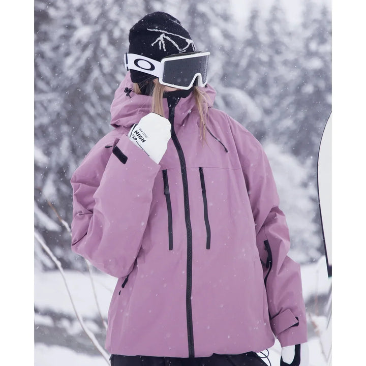 Tæt udsnit af model i lyslilla jakke med hætte, skibriller og hvide handsker, der løfter den ene hånd mod ansigtet i snevejr. 4