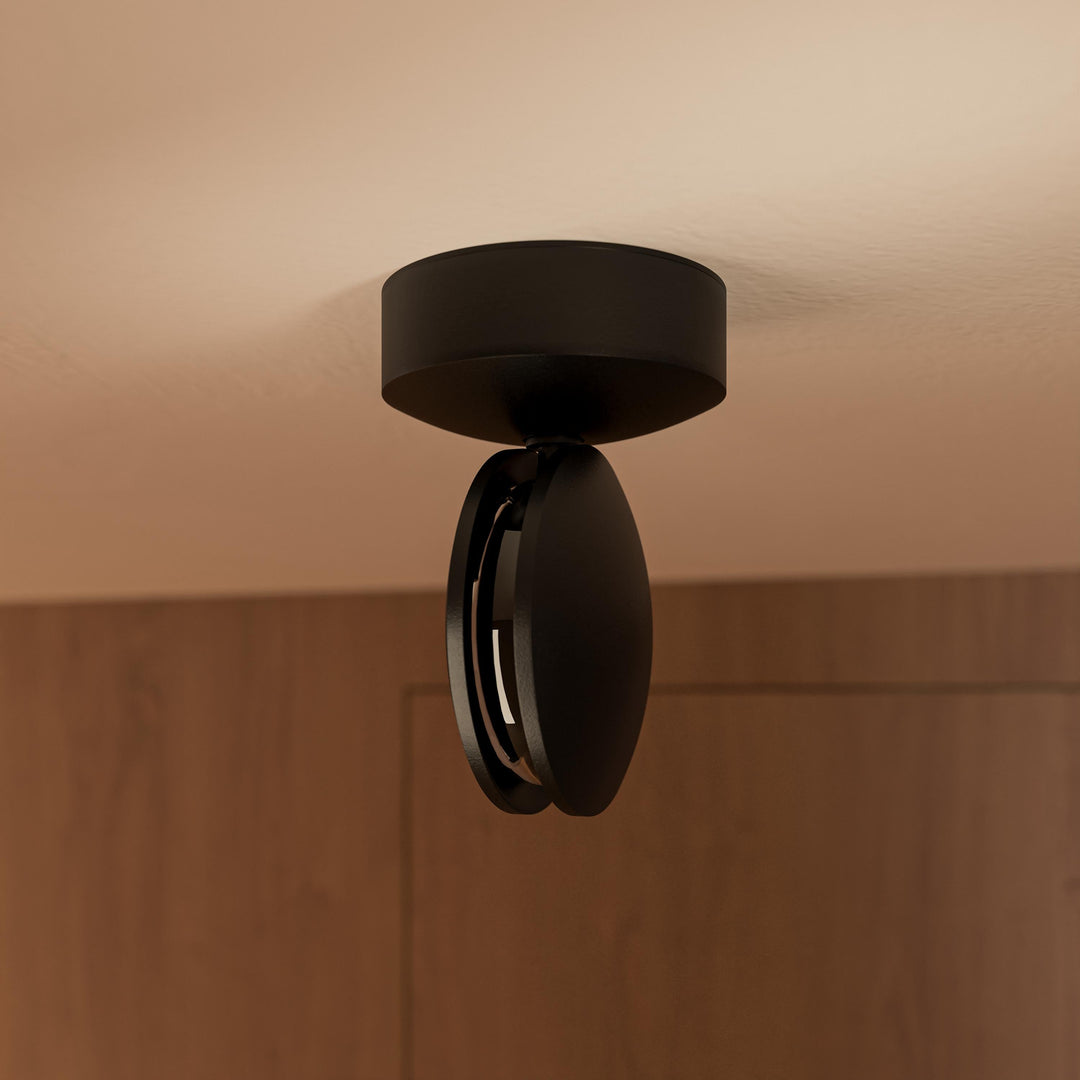 Sort loftlampe set skråt nedefra, hvor det drejede runde hoved med den indre lyskilde og sokkel på loftet tydeligt ses. 13