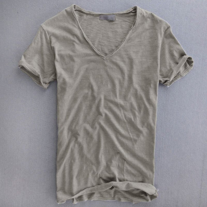 Kortærmet T-shirt med V-udskæring i grå, lagt fladt på en grå baggrund, med let struktureret stof og oprullede ærmekanter. 1