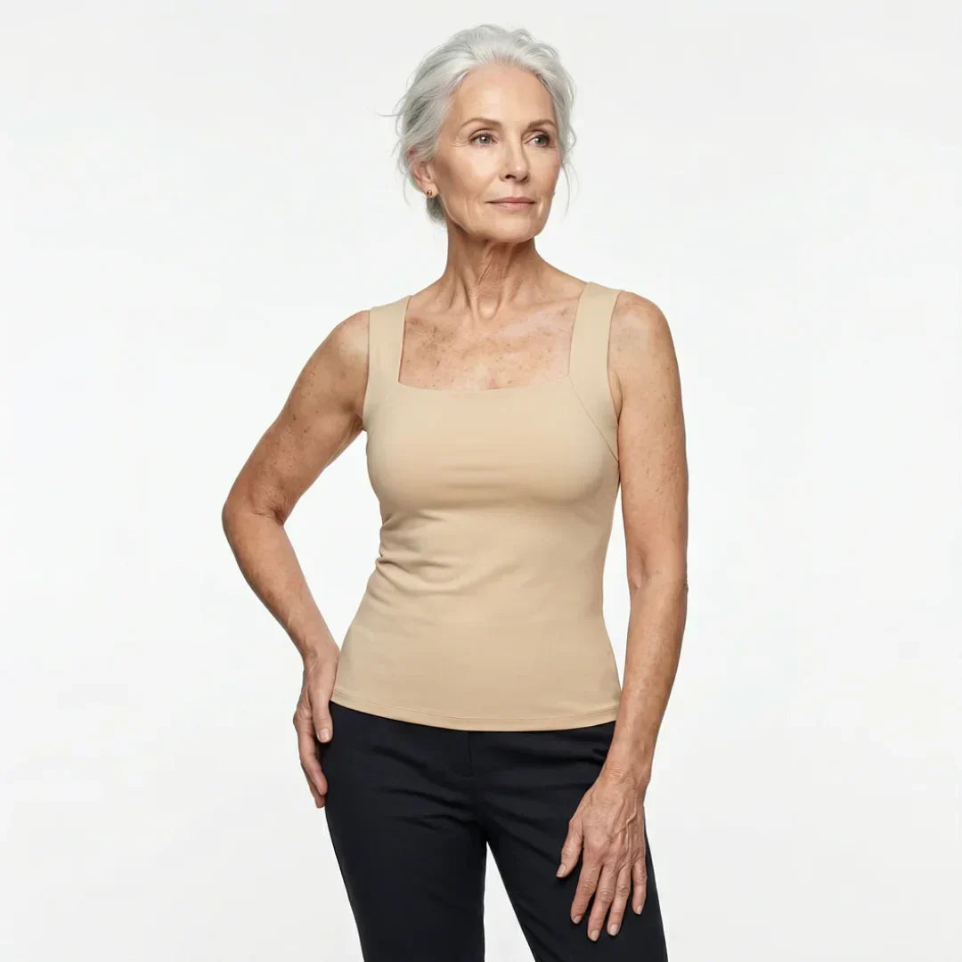 Kvinde med sat grå hår i beige tanktop med firkantet udskæring og sorte bukser, set skråt forfra mod hvid baggrund. 8