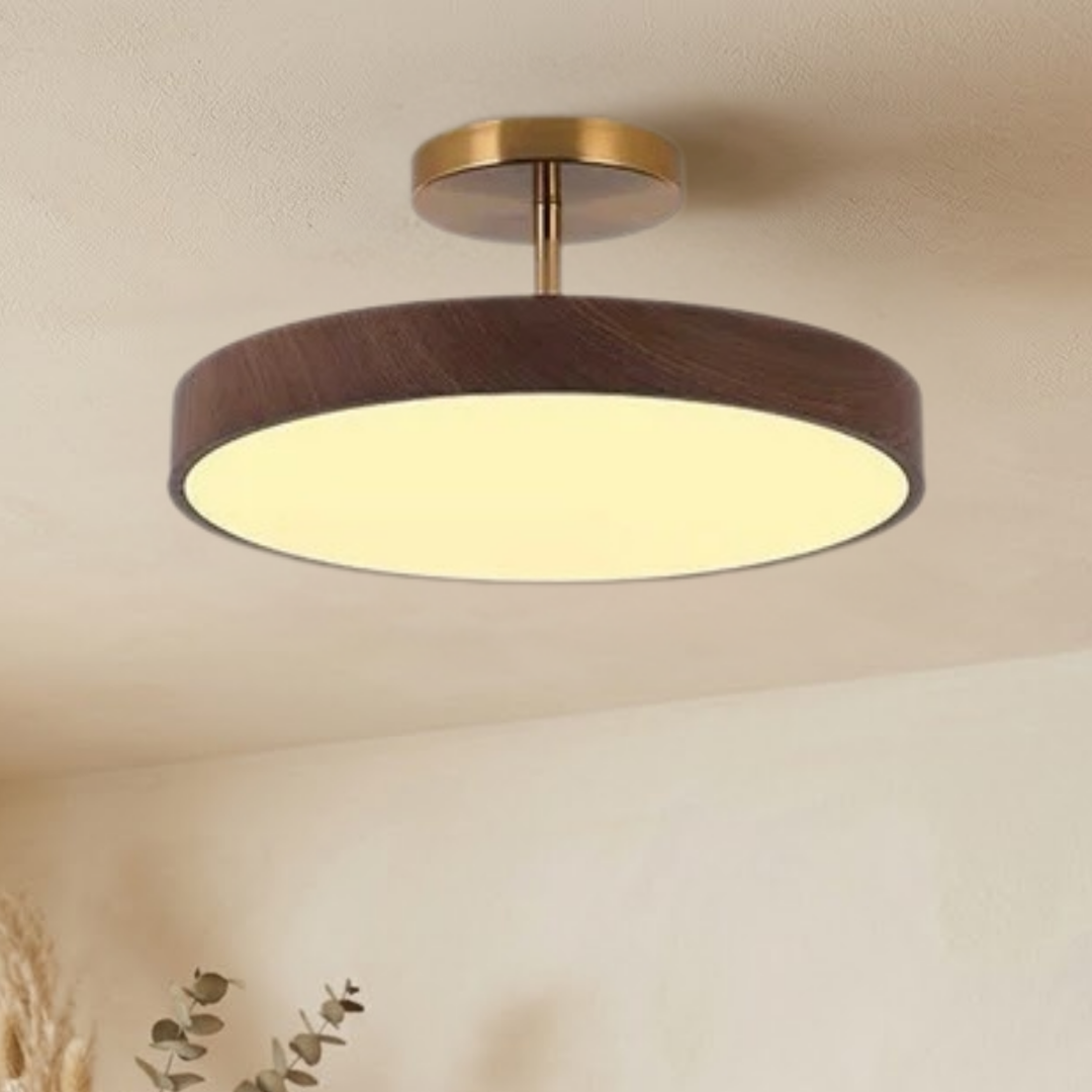 Tændt lampe med mørkt trælook og guldfarvet stel set nedefra og lidt fra siden, med varmt lys og dekorationsgrene i hjørnet. 3