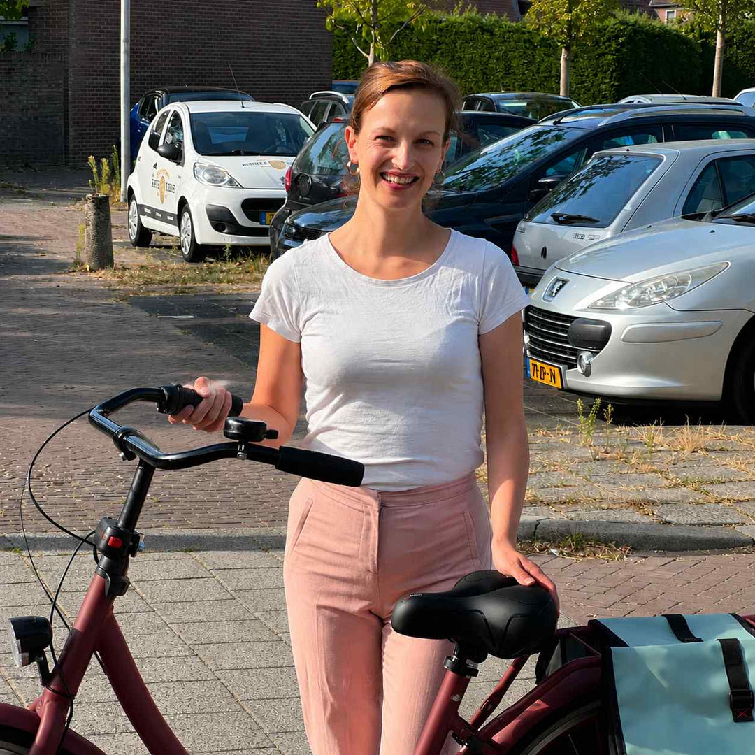 Smilende kvinde står ved en rød cykel med den sorte brede sadel, og lægger hånden på sædet. 7