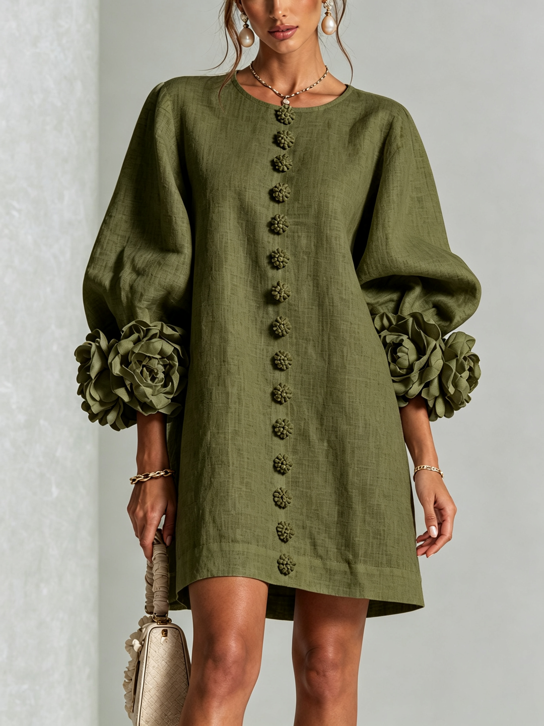 Olivengrøn minikjole set forfra med blomsterknapper, brede pufærmer og store rosmanchetter, model holder lille taske. 7