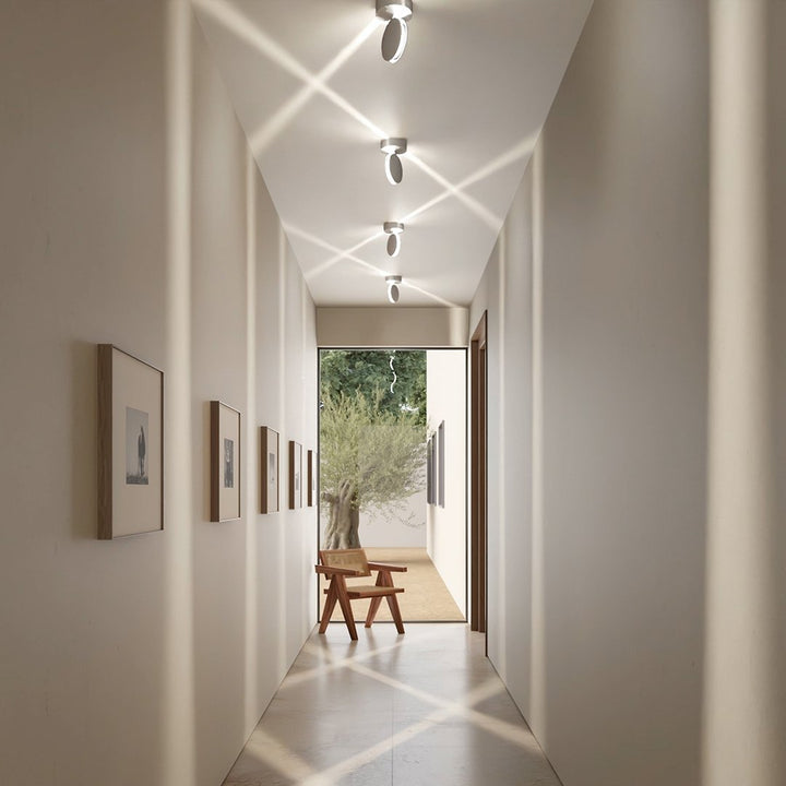 Gang med hvide loftlamper, der kaster krydsende diagonale lysstråler på loftet og bløde lyssøjler på væggene. 7