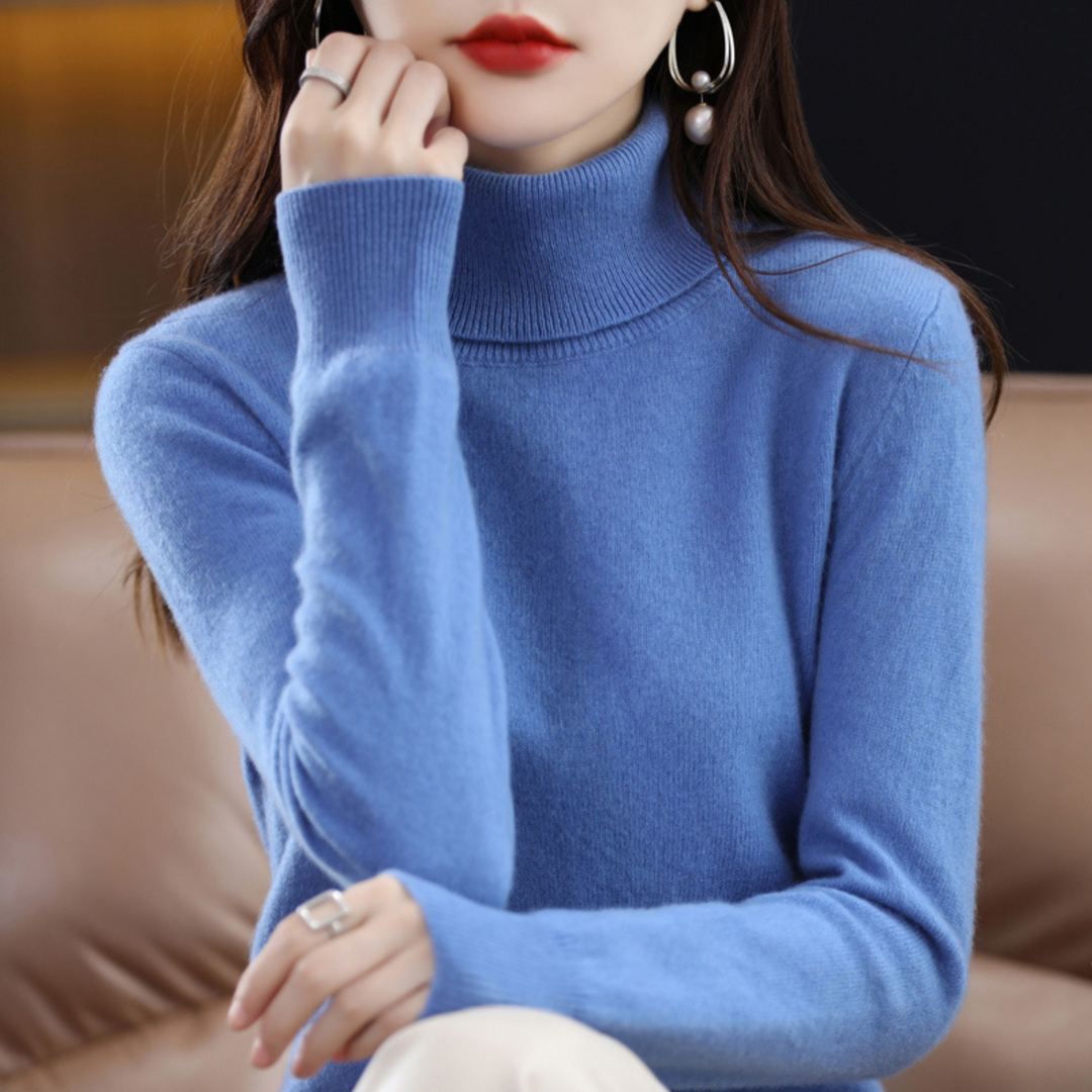 Model i blå rullekravesweater med hånden hvilende mod kinden, siddende i en brun lædersofa. 3
