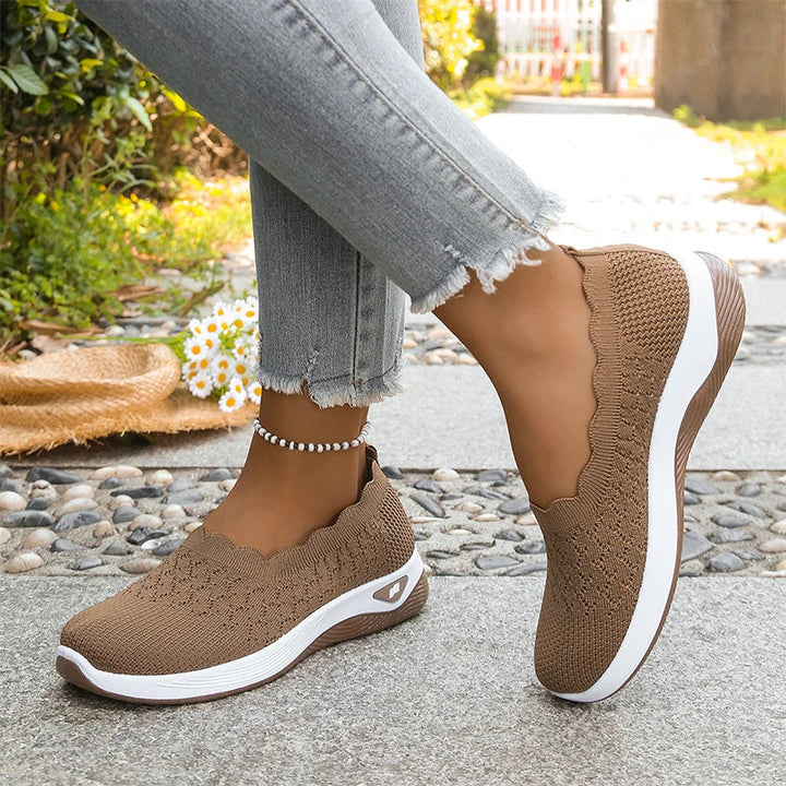 Brune strikkede slip-on-sko med bølgekant og hvid mellemsål, båret på en sti med småsten 20