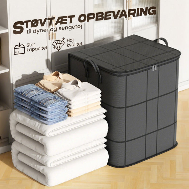 Sort opbevaringstaske med hanke og lynlÃ¥s ved siden af stablede dyner, jeans og skjorter foran et hvidt skab. 6