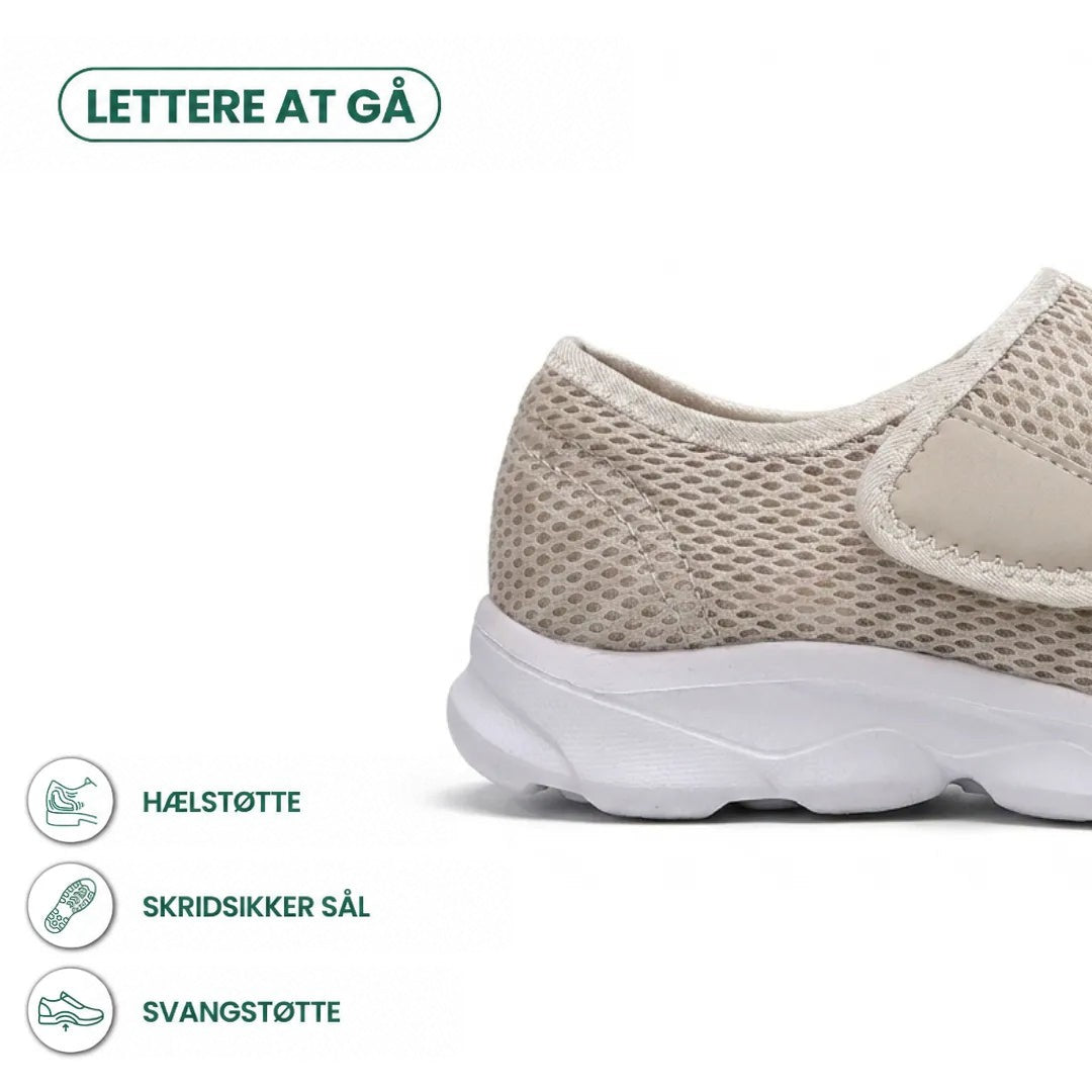 Beige mesh-sko set fra siden med fokus på hælen, velcrostroppen og den tykke hvide sål, med ikoner for støtte og skridsikkerhed. 31