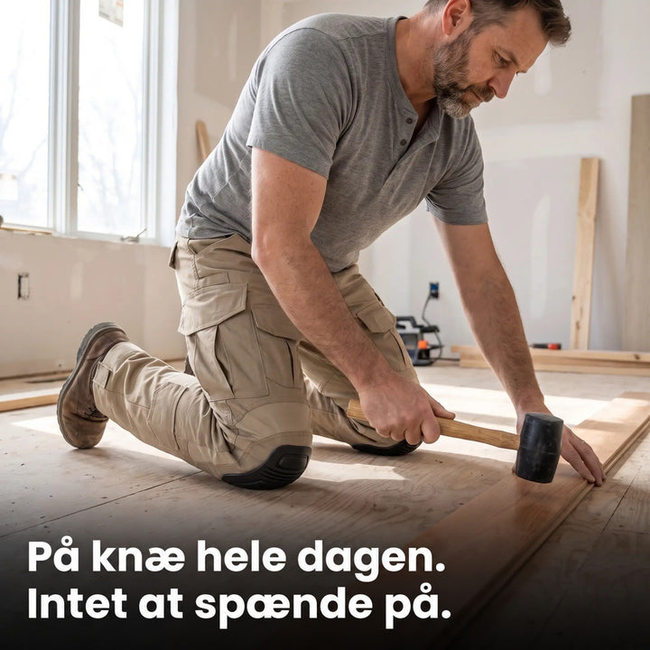 Mand i beige arbejdsbukser knæler på et råt trægulv og banker en gulvplanke på plads med en gummihammer. 3