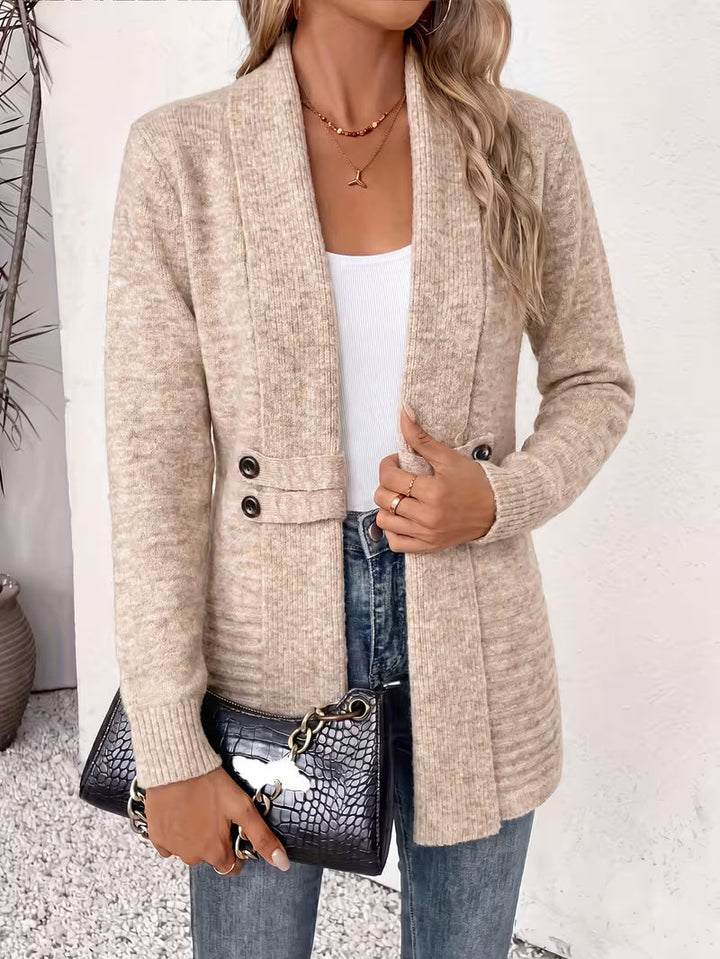 Kvinde i beige cardigan med sjalskrave, hvid top og jeans, holder en sort taske 3