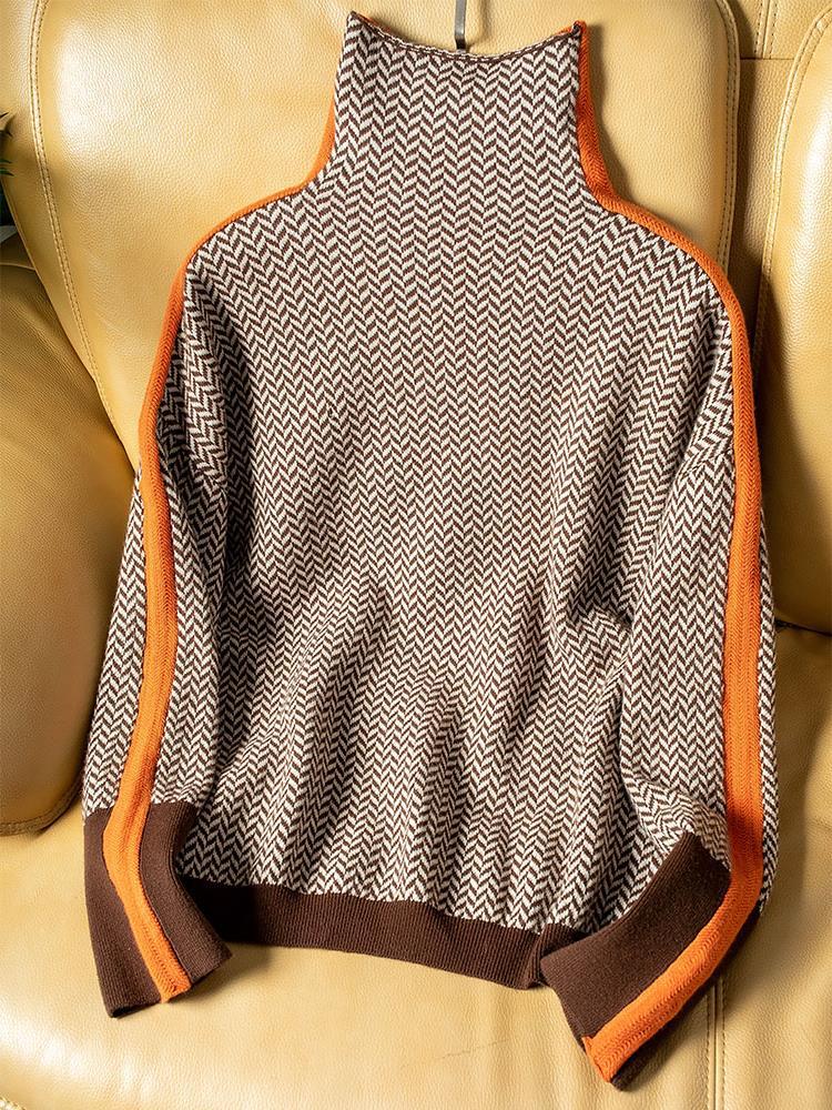 Sweateren i brun og creme med orange striber langs ærmerne ligger flat på en gul lædersofa. 4
