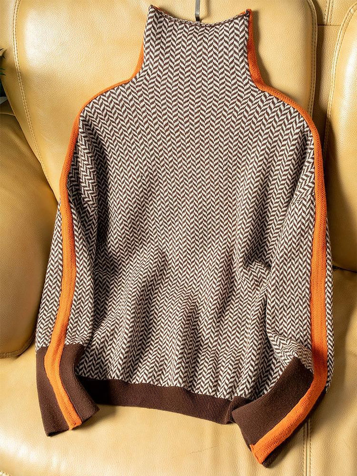 Sweateren i brun og creme med orange striber langs ærmerne ligger flat på en gul lædersofa. 4