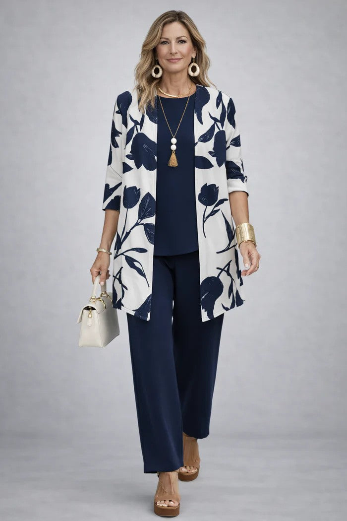 Model i hvid cardigan med store marineblå blomster og blade over marineblå top og vide marineblå bukser. 15
