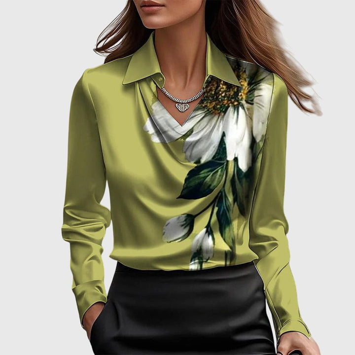 Model i grøngul satinbluse med stort hvidt blomsterprint og grønne blade ved vandfaldsudskæringen, med sort nederdel. 7