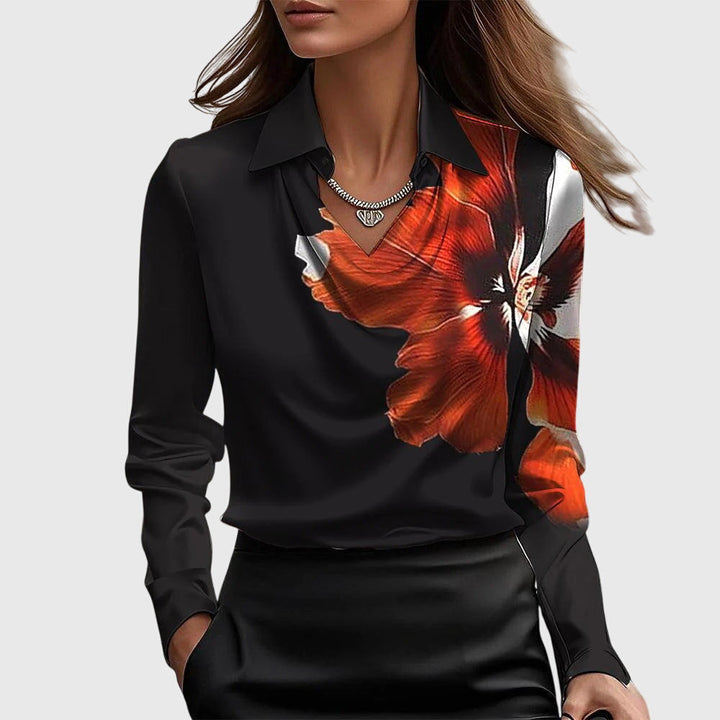 Model i sort satinbluse med stort rødorange blomsterprint over skulder og bryst, vandfaldsudskæring og krave. 6