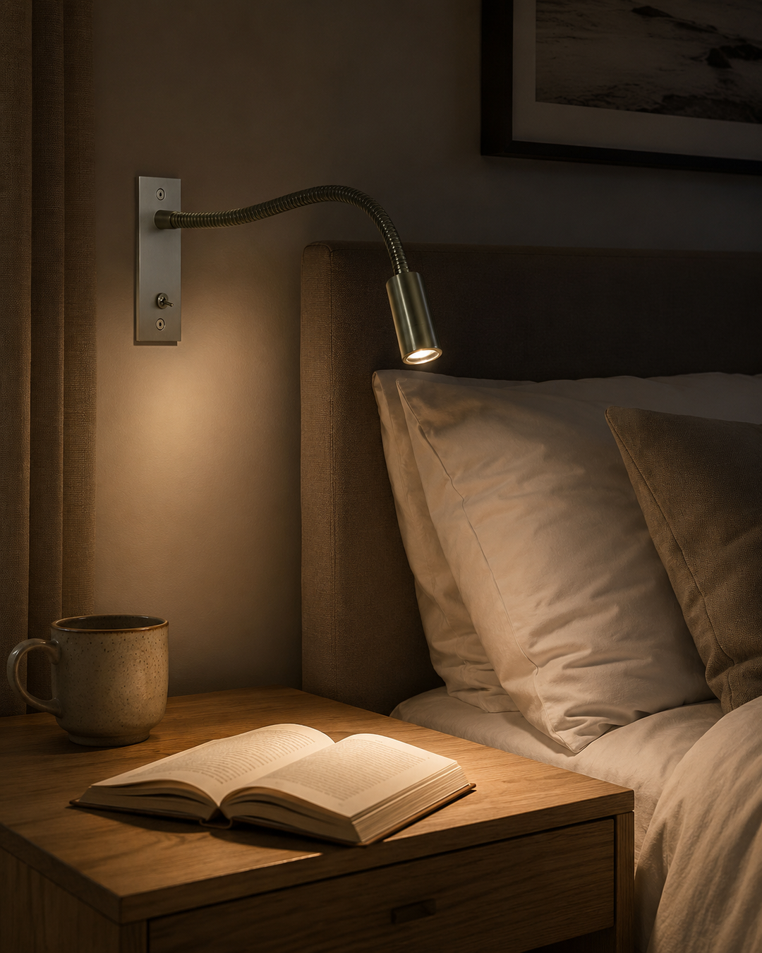 Lampe i børstet nikkel tændt over sengegavlen, mens lyset falder på en opslået bog og et keramikkrus på natbordet. 8