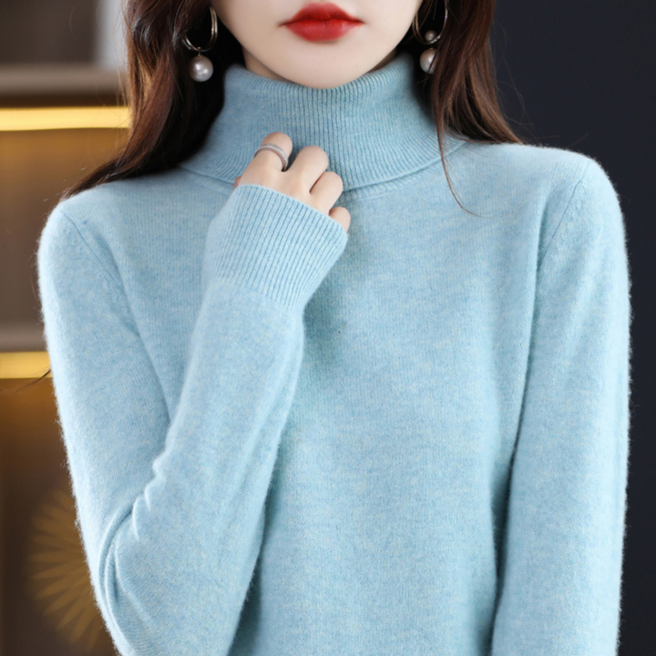 Model i lyseblå rullekravesweater med ribstrikket krave og manchet, mens hun rører ved kraven. 4