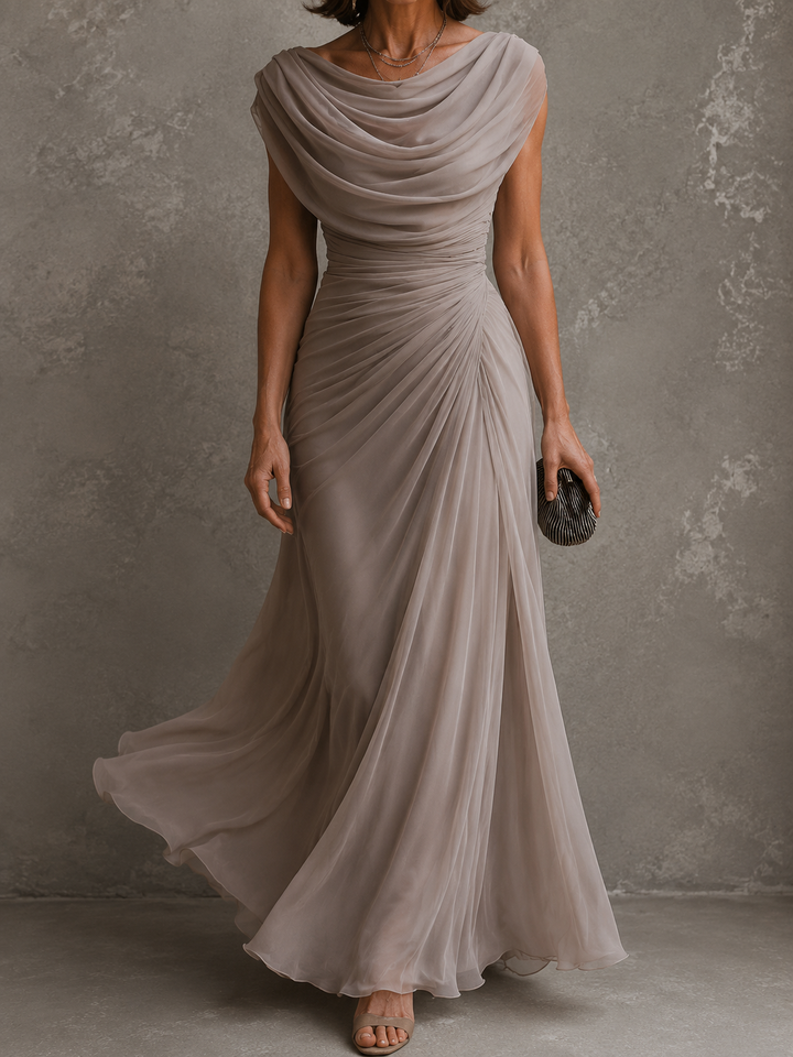 Model i gråbeige maxikjole i bevægelse, hvor det lette, flagrende skørt og draperingen over brystet fremhæves. 8