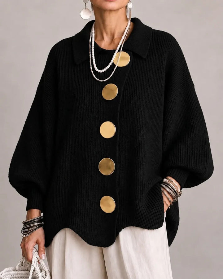 Model i sort ribstrikket cardigan med store guldfarvede knapper og spids krave, båret med hvide bukser. 8