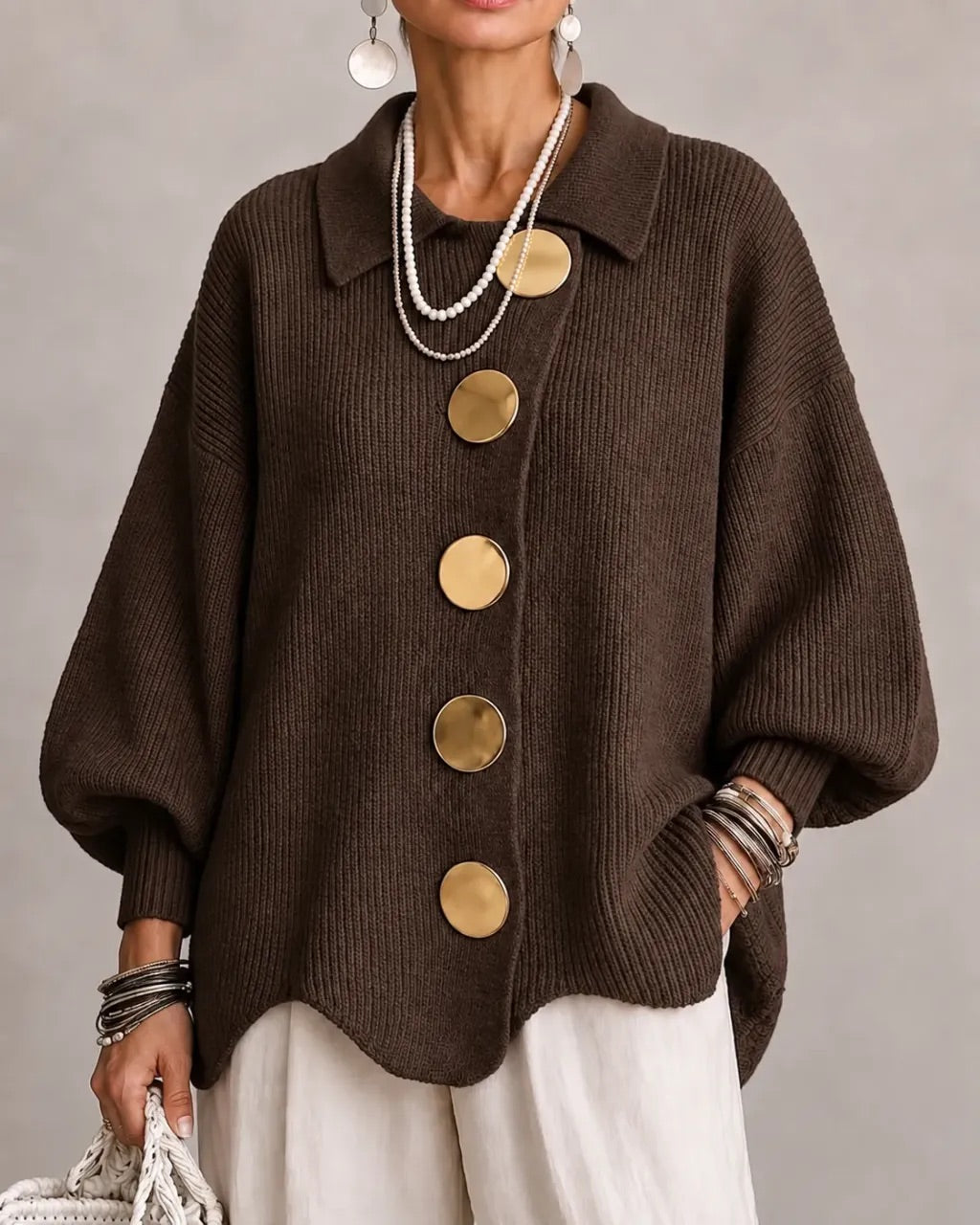 Model i mørkebrun ribstrikket cardigan med store guldfarvede knapper, bølgekant og brede ærmer, set forfra. 9