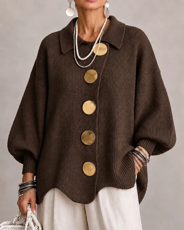 Model i mørkebrun ribstrikket cardigan med store guldfarvede knapper, bølgekant og brede ærmer, set forfra. 9