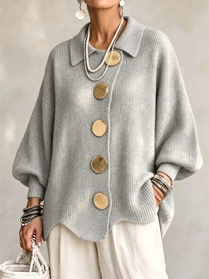 Model i lysegrå ribstrikket cardigan med store guldfarvede knapper og bølgekant, båret med hvide bukser. 10