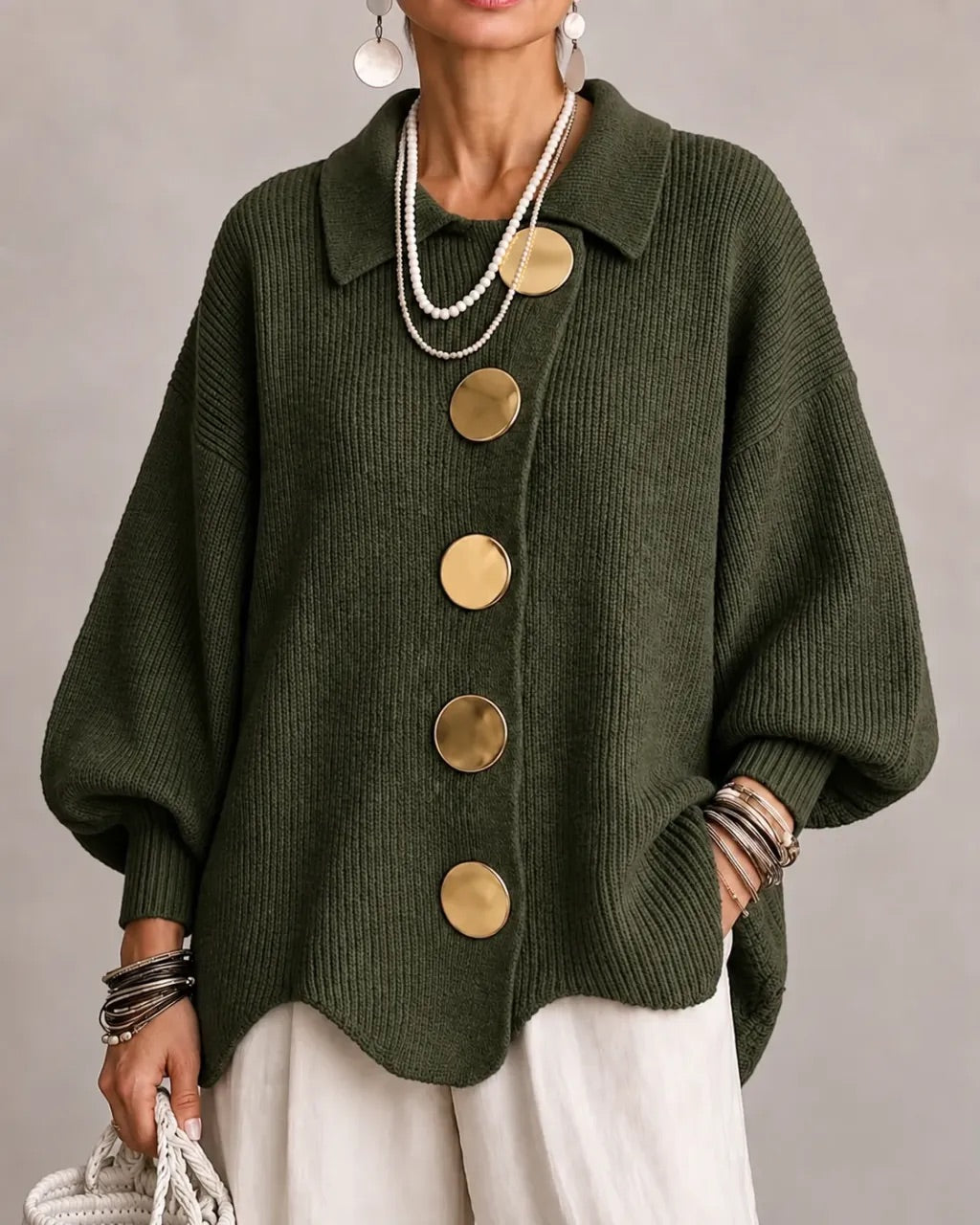 Model i mørkegrøn ribstrikket cardigan med store guldfarvede knapper og spids krave, båret med hvide bukser. 12