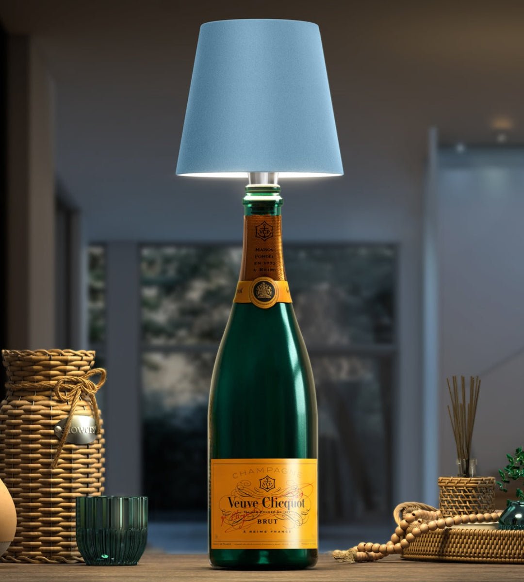 Lyseblå lampeskærm på en grøn champagneflaske, med fletkurve og perlekæde som indretning på bordet omkring. 6