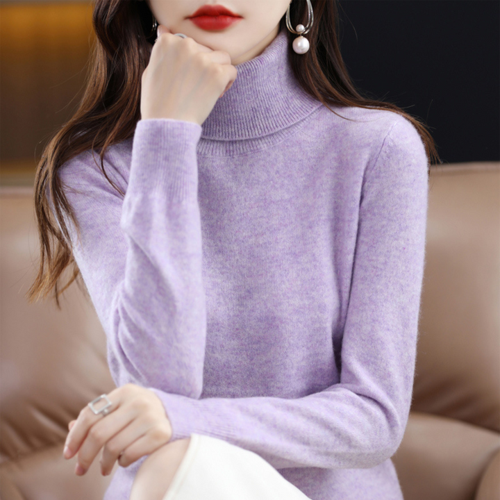 Model i lys lavendelfarvet rullekravesweater med hånden op mod hagen, siddende i en sofa. 6