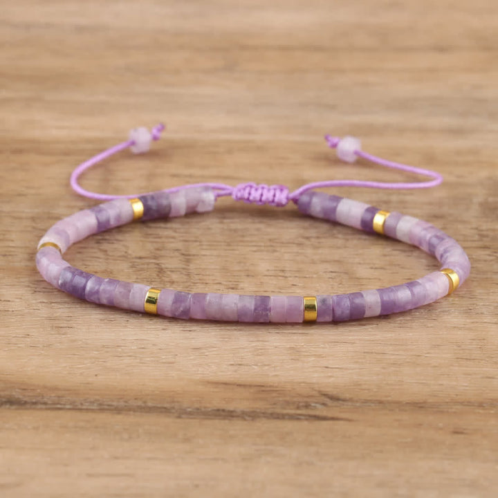 Lila Armband aus Amethyst und Goldperlen, verstellbar, handgefertigt, auf Holzuntergrund.
