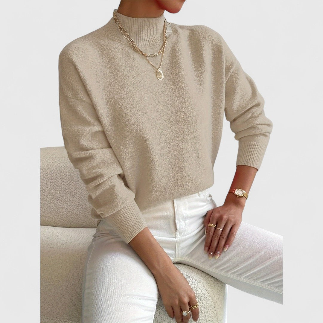 Model i beige strikbluse med ribstrikket krave og manchetter, siddende afslappet i hvide bukser med guldsmykker. 7
