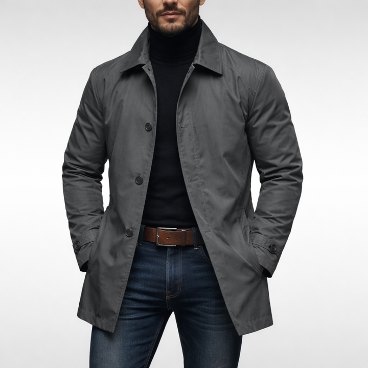 Samme grå frakke set forfra på model med sort rullekravetrøje, mørke jeans og brunt læderbælte. 2