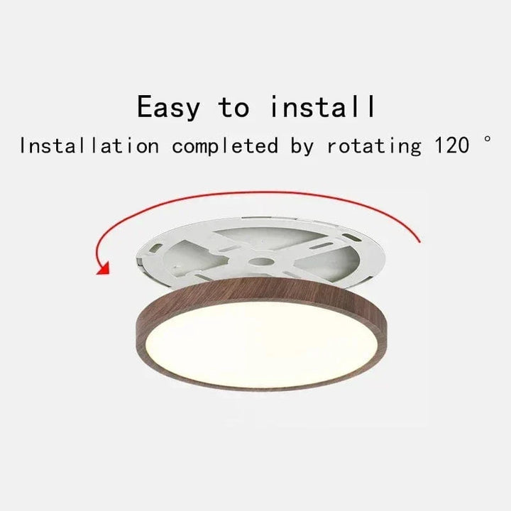 Loftlampen med mørk træfinish set skråt nedefra, med monteringsbeslaget løftet over lampen og en rød pil, der viser drejning ved montering. 1