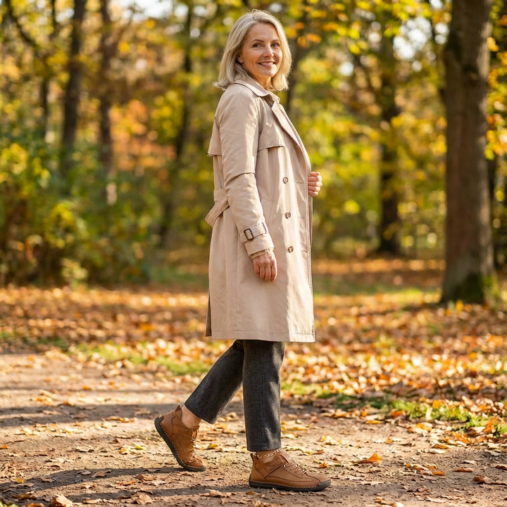 Kvinde i trenchcoat går på en sti med efterårsblade, iført brune sko set fra siden. 18