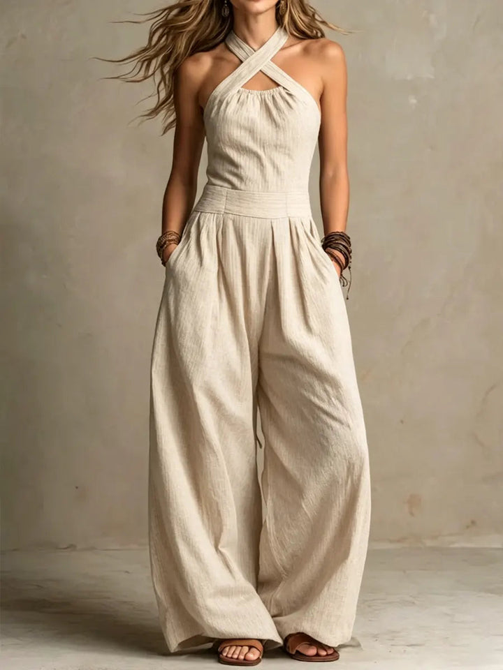 Model i den samme jumpsuit i lys beige med krydsede halsstropper, lommer og vide ben, set forfra. 2