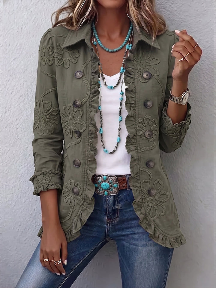 Model i olivengrøn jakke med broderede blomster og flæsekant, båret med hvid top og jeans 1