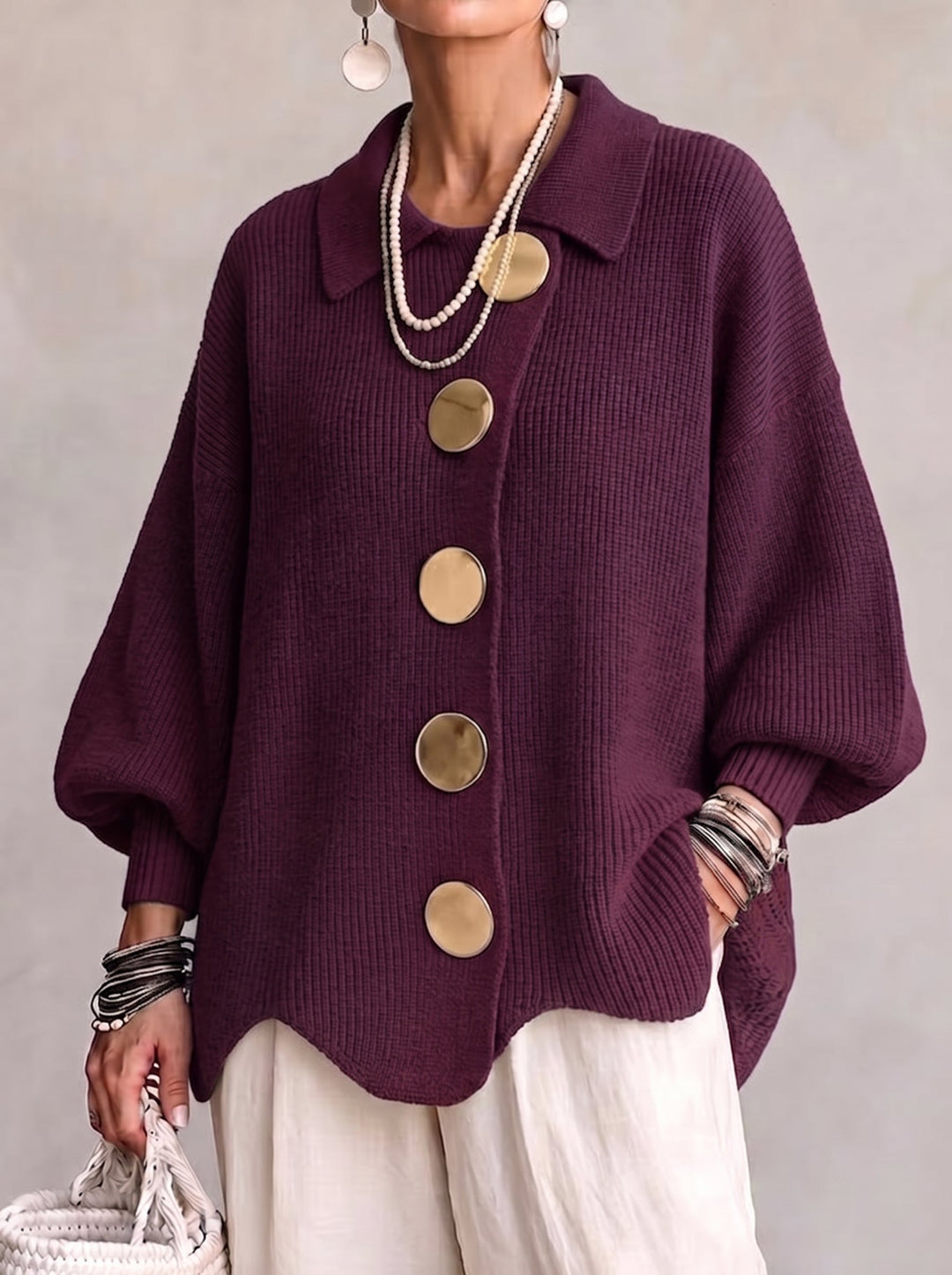 Model i blommefarvet ribstrikket cardigan med spids krave og store guldfarvede knapper, set forfra med hvide bukser. 2